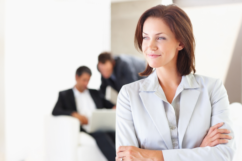 An attractive young business woman looking away with colleagues working behind. Delegate.